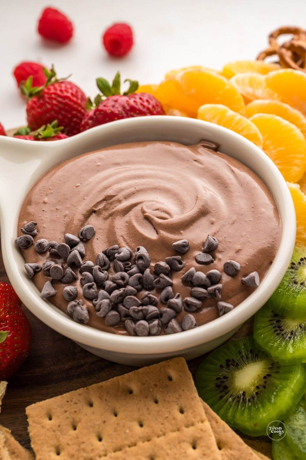 Bowl full of creamy chocolate dip with fruit and crackers.