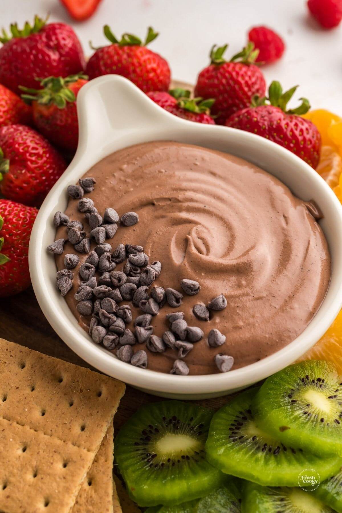 Chocolate fruit dip sprinkled with mini chocolate chips surrounded by fruit and graham crackers.