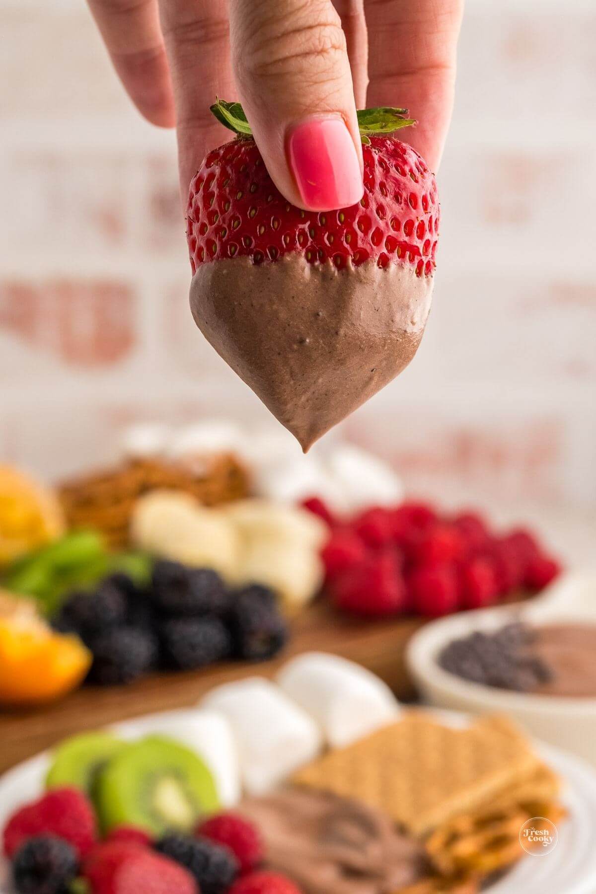 Hand dipping ripe strawberry into chocolate fruit dip.