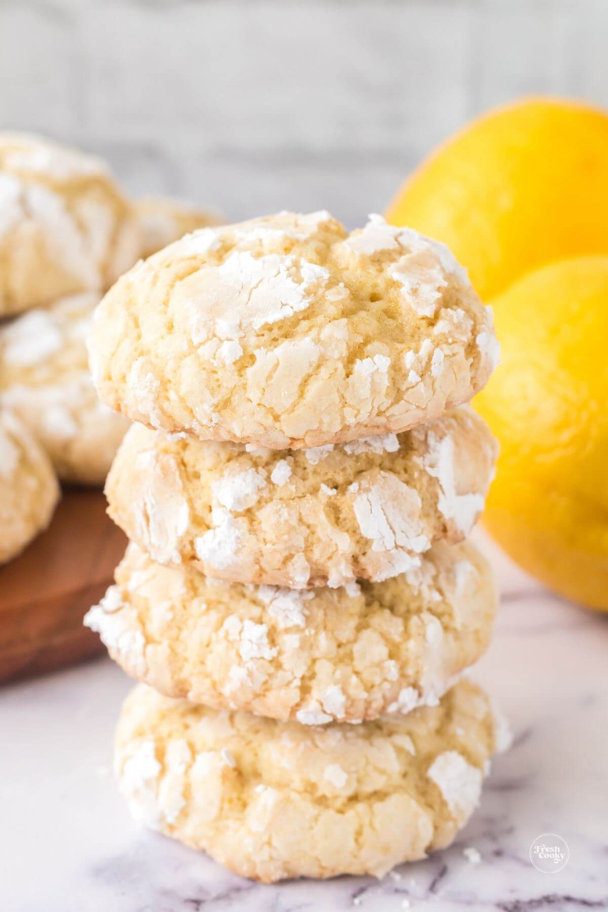 Stacked lemon crinkle cookies with fresh lemons behind.