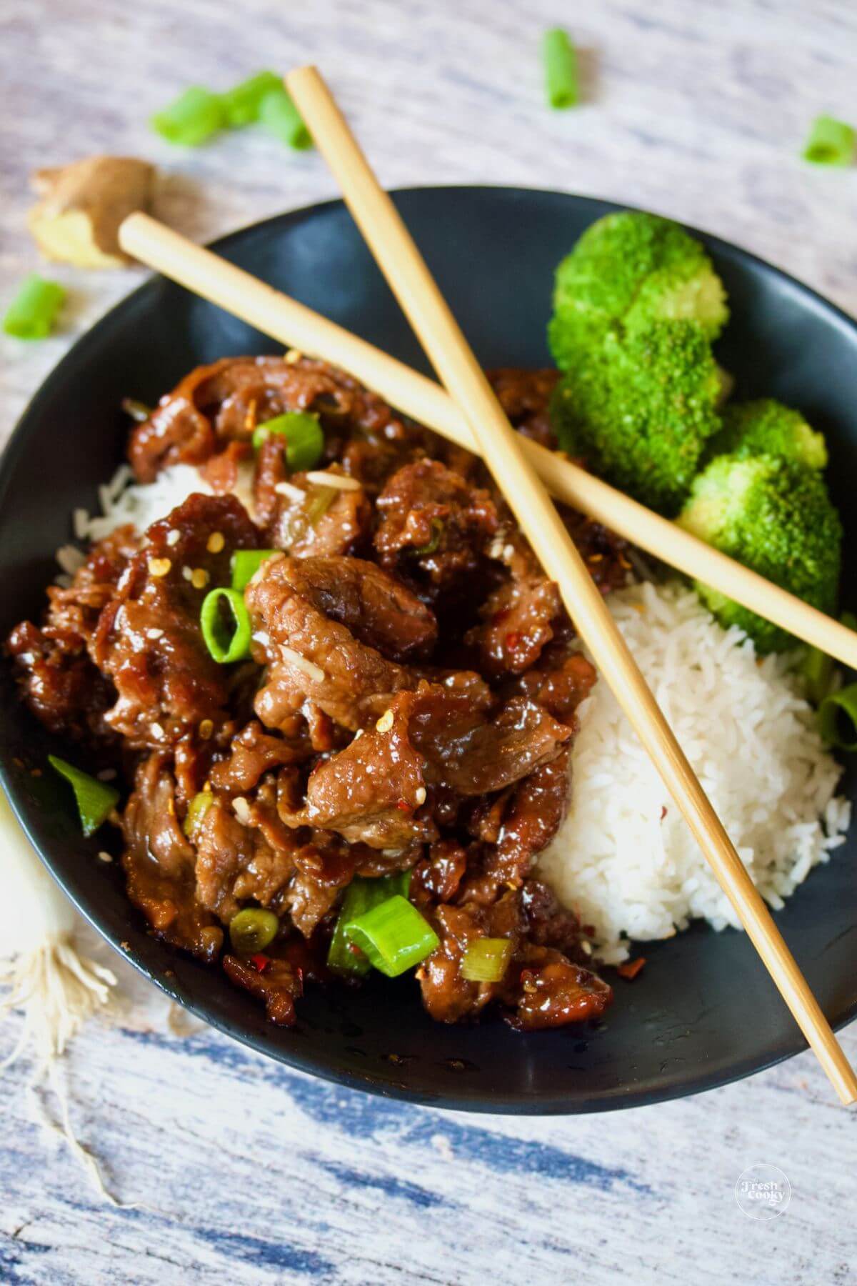 A bowl of mongolian beef made with shaved steak on top of white rice and steamed broccoli.