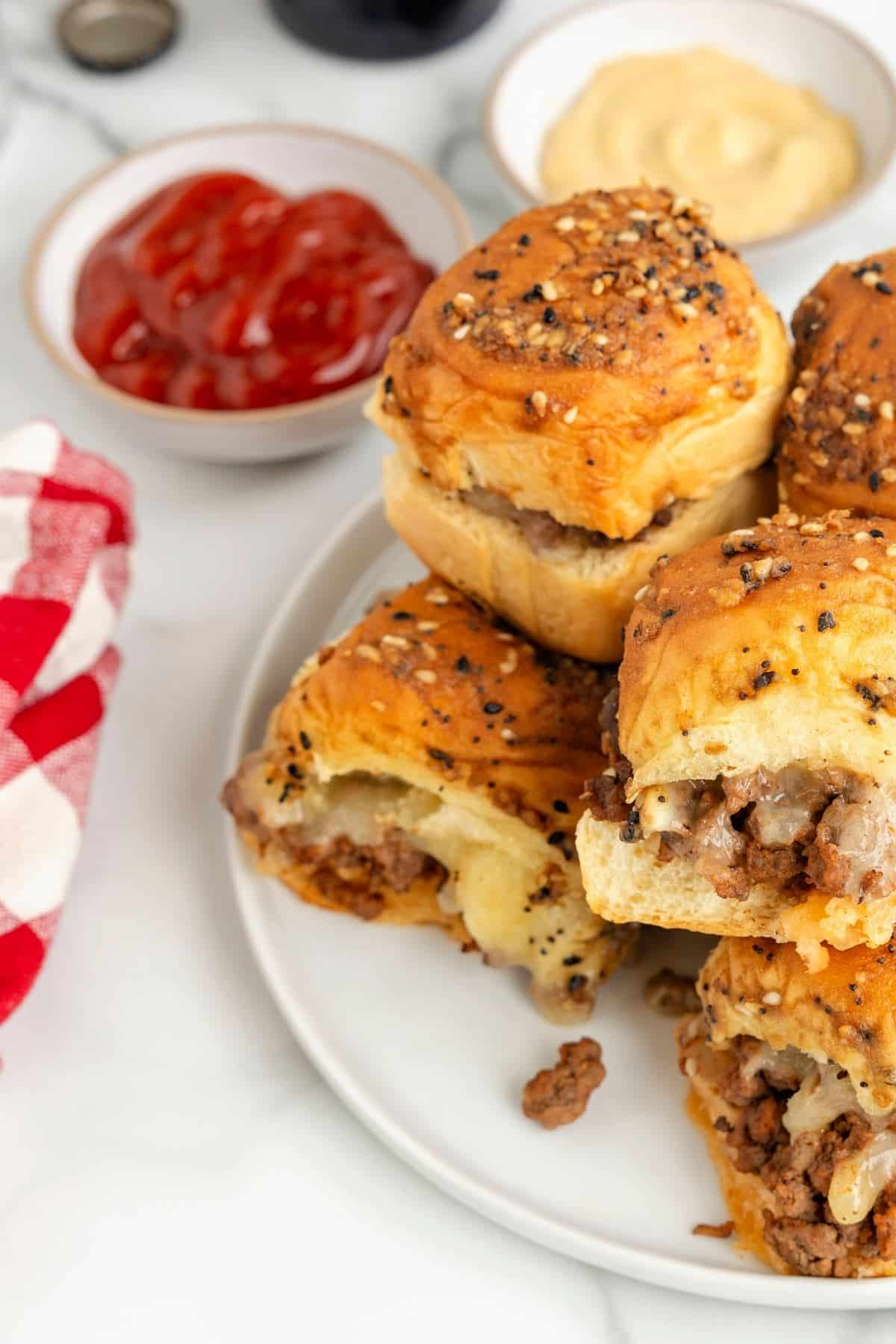 Cheeseburger sliders on plate with ketchup and dipping sauces behind. 