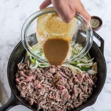 Pour the steak seasoning sauce onto the shaved steak in the pan.