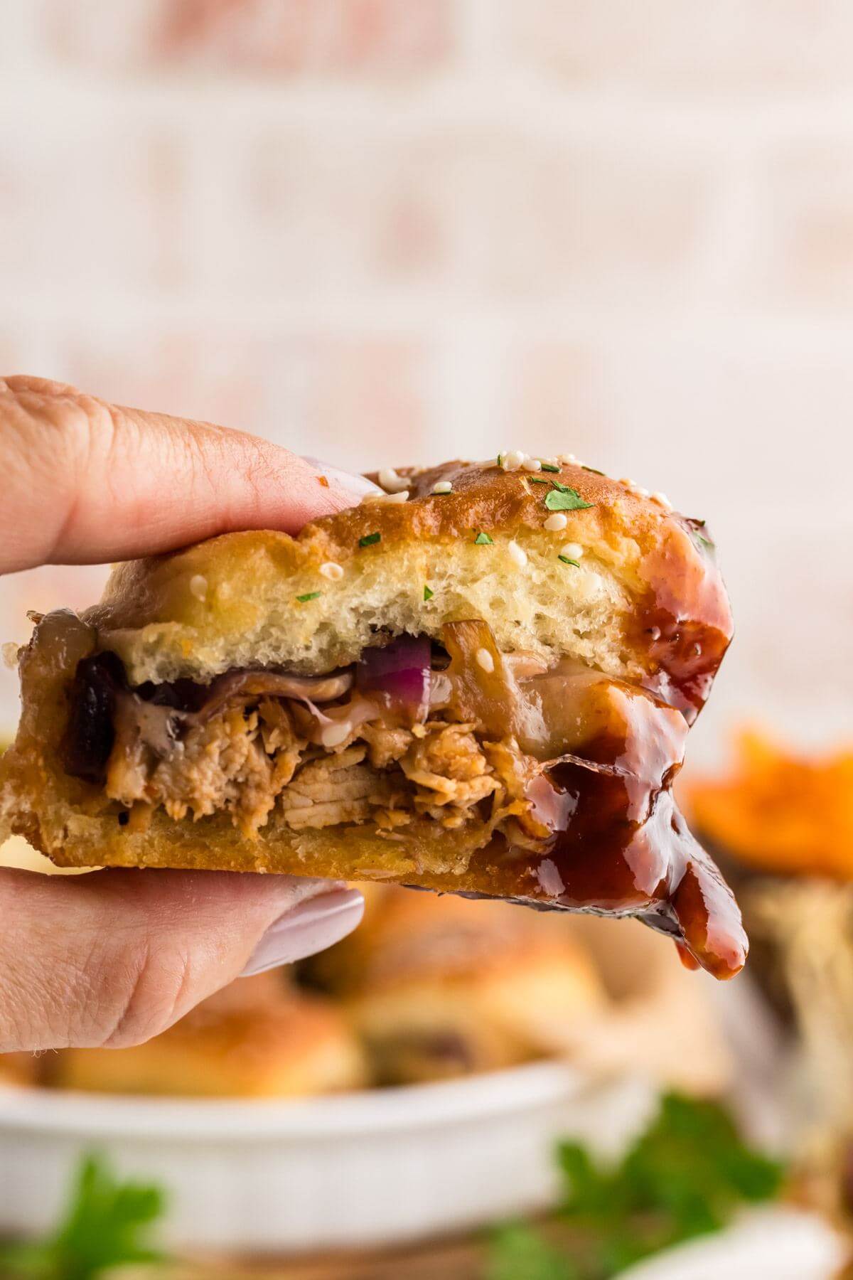 Close up view of someone holding a BBQ Chicken Slider dripping BBQ sauce.