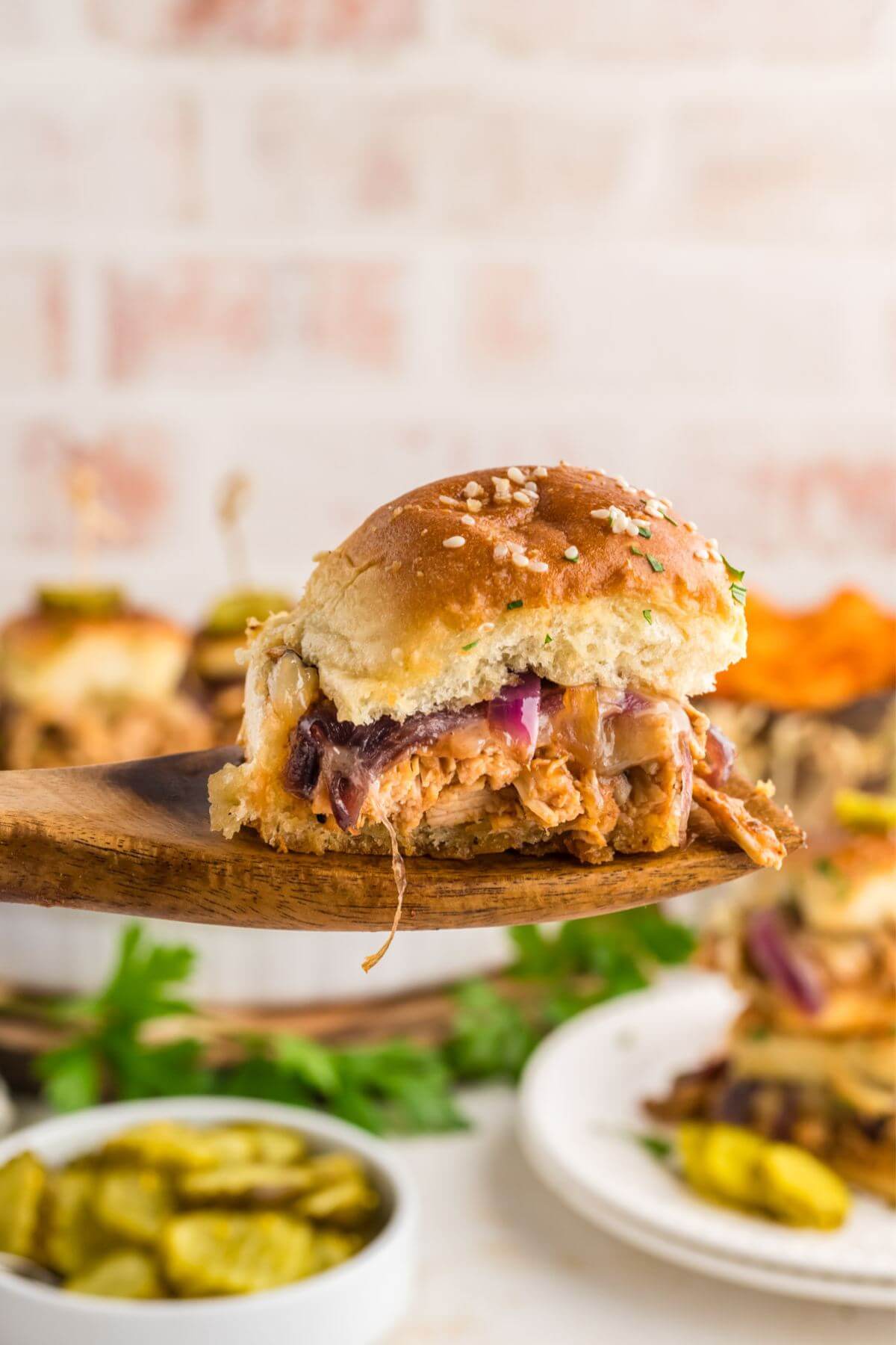 BBQ Chicken Sliders in background with centered focus on slider lifted on a wooden spoon showing filling.