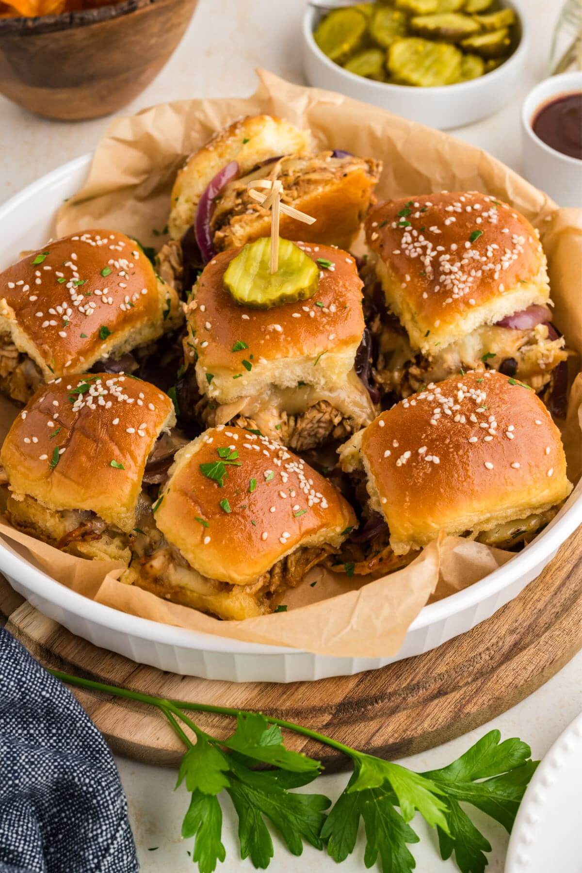 Barbecue Chicken Sliders grouped in round dish with a pickle on top of the center slider.