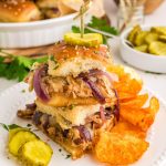 Stacked Barbeque Chicken Sliders topped with pickle and served with chips on plate.