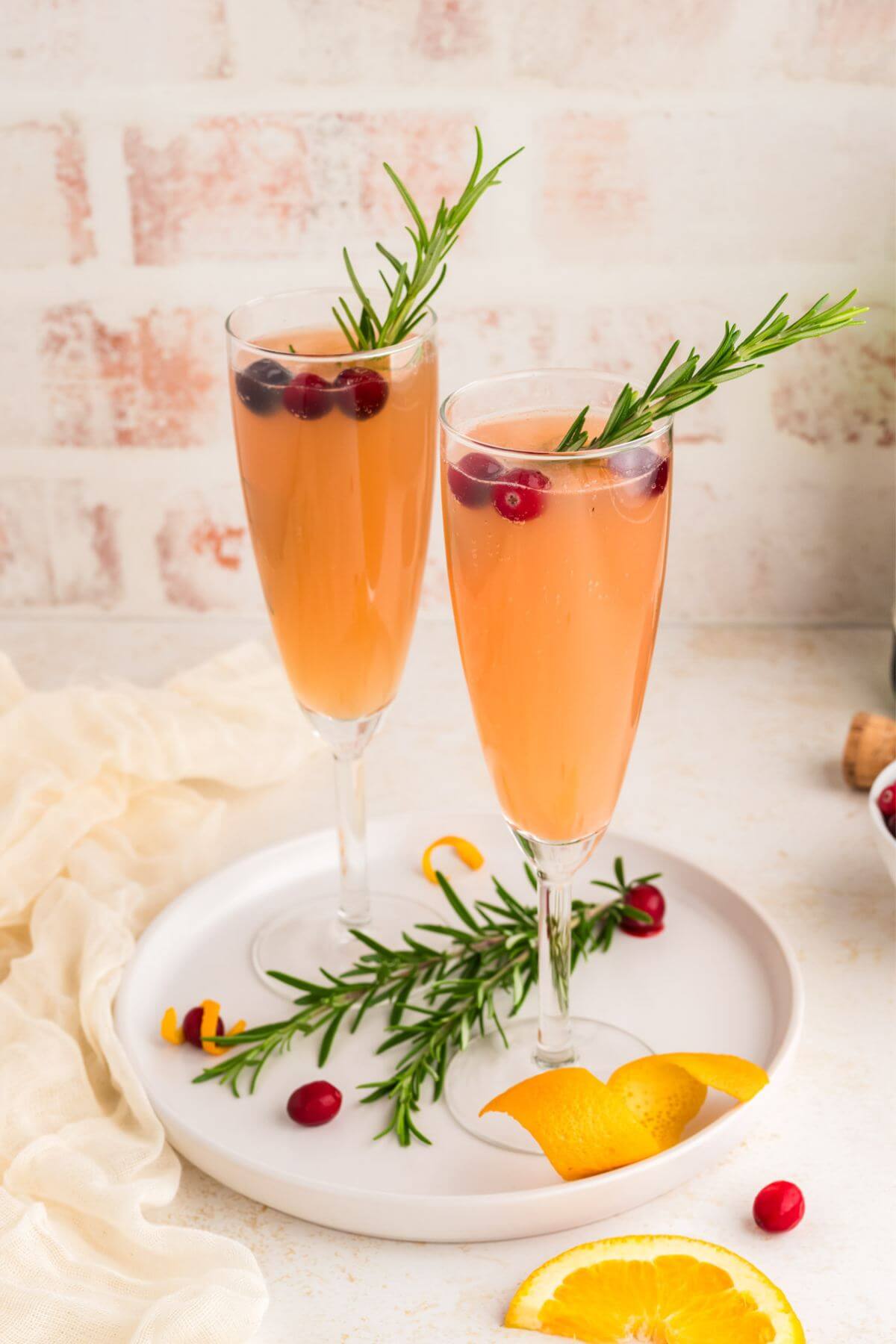 Two flutes of Christmas Mimosa with orange peel, cranberries and rosemary garnishes.