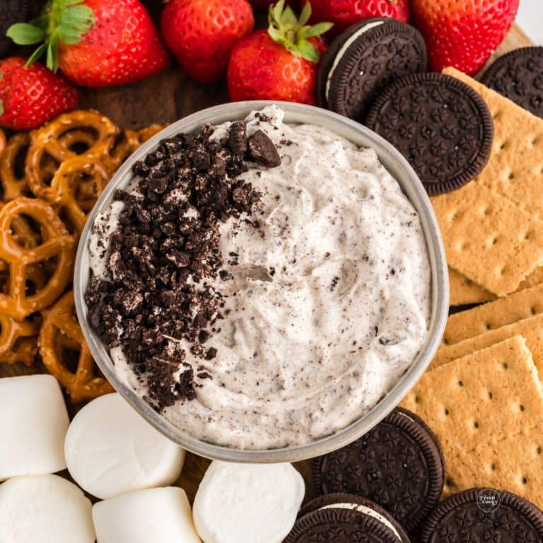 A bowl of fluffy, sweet Oreo fluff on a tray surrounded by strawberries, graham crackers, pretzels, marshmallows and graham crackers.