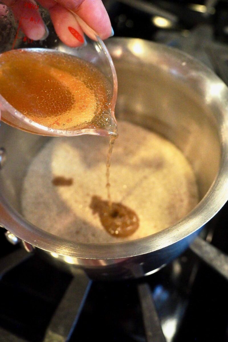 Adding ham juices and bourbon to sugar spice mixture in pan on stove.