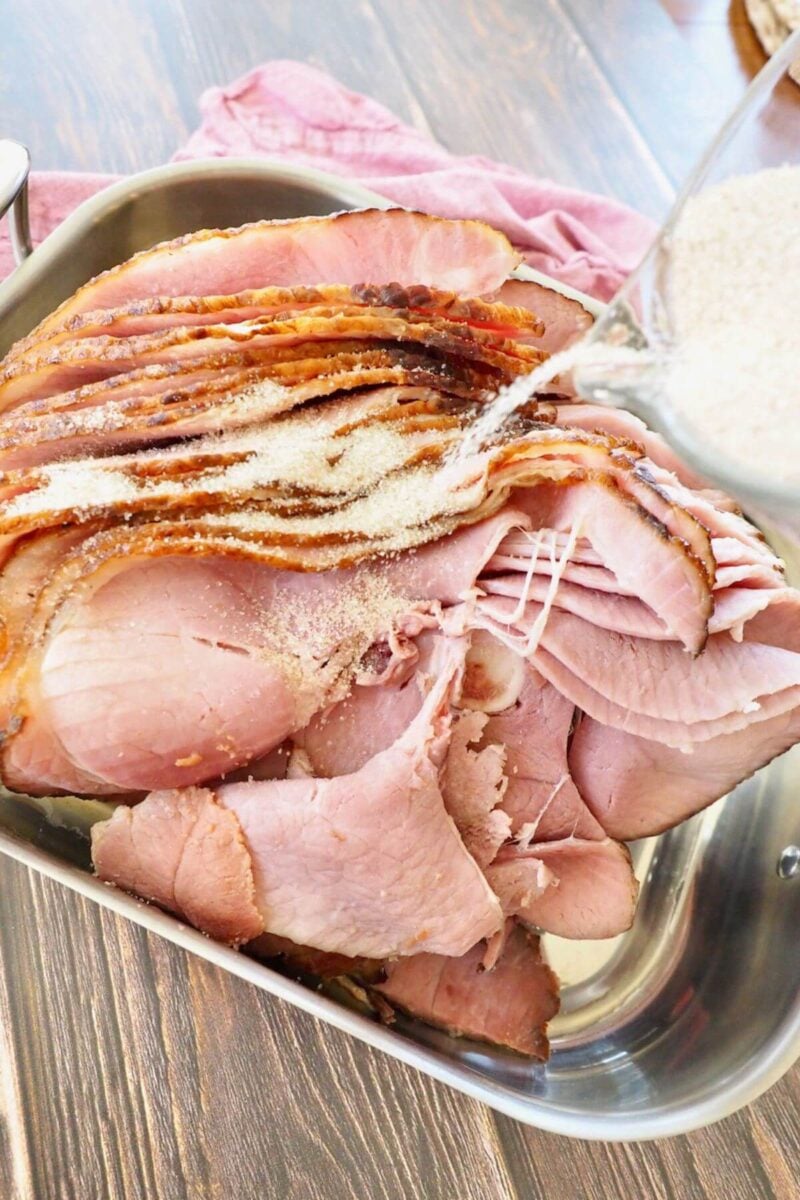 Pouring spiced sugar mixture over top of warmed ham in roasting pan to go into oven.