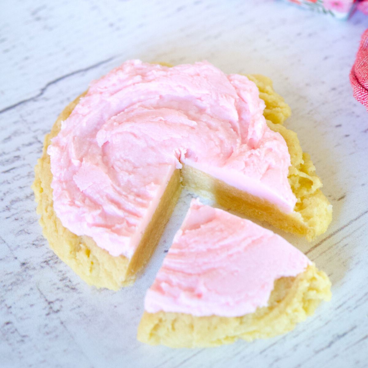 A large Copycat Crumbl Sugar Cookie with almond icing with ¼ wedge cut out.