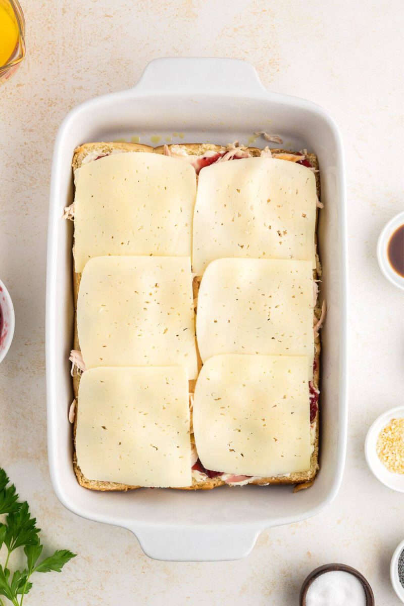 Cheese layer spread on rolls for easy baked turkey sliders.