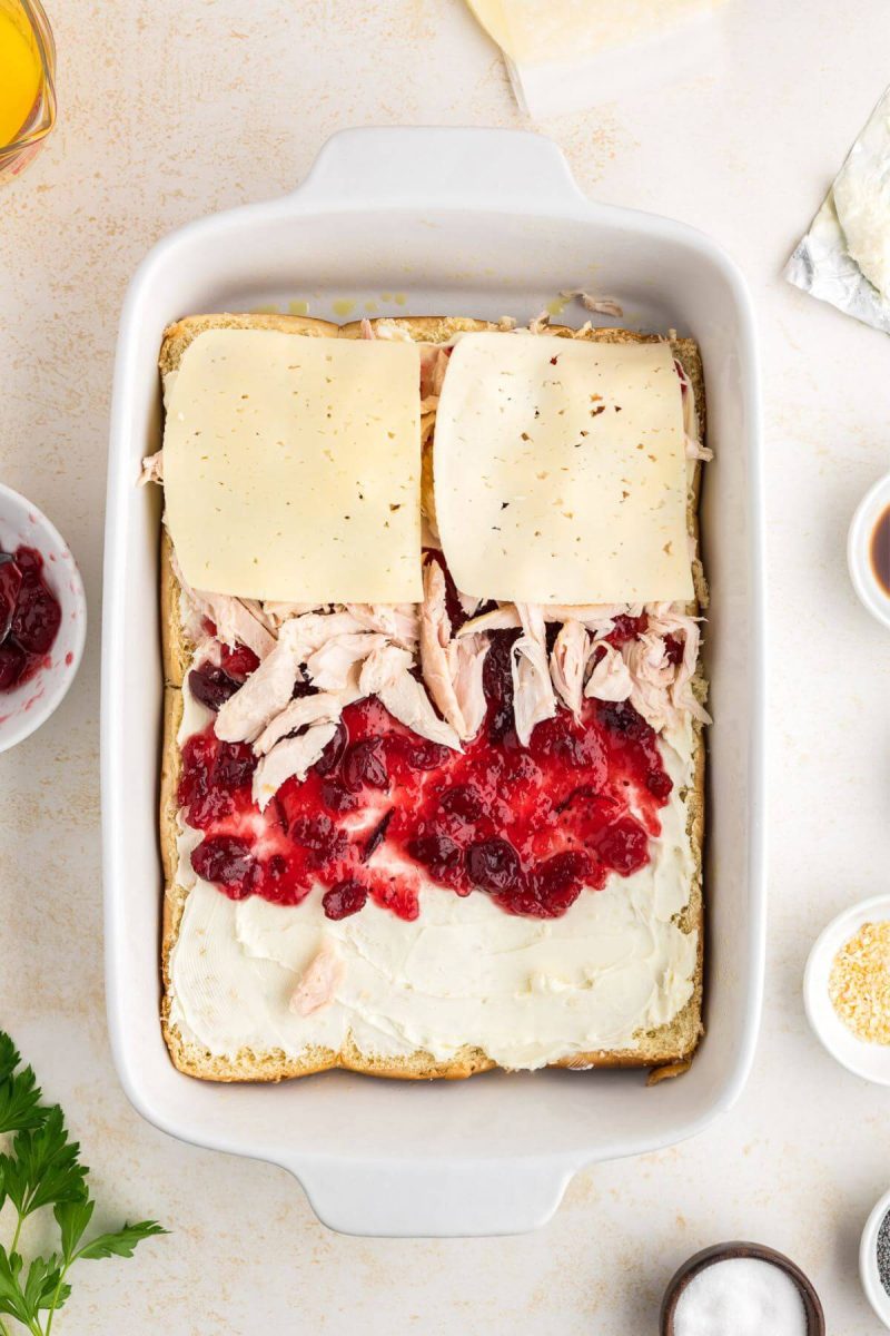 Easy baked turkey sliders with cream cheese, cranberry sauce, turkey and cheese layers shown.