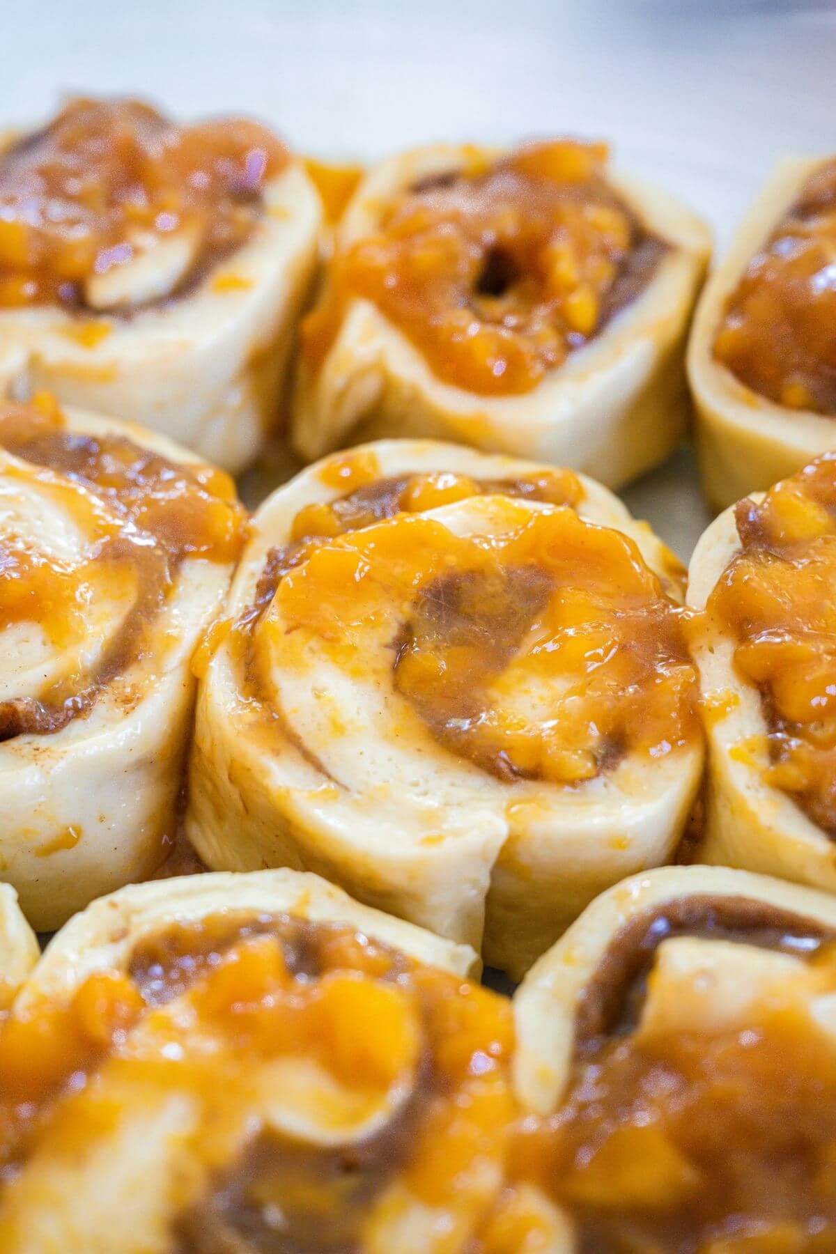 Close up of peach cinnamon rolls raising in pan with extra peach jam spooned on top. 