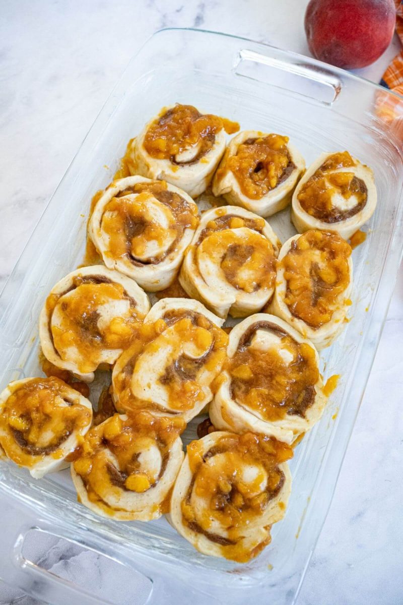 Sliced cinnamon rolls with peaches in glass baking dish. 