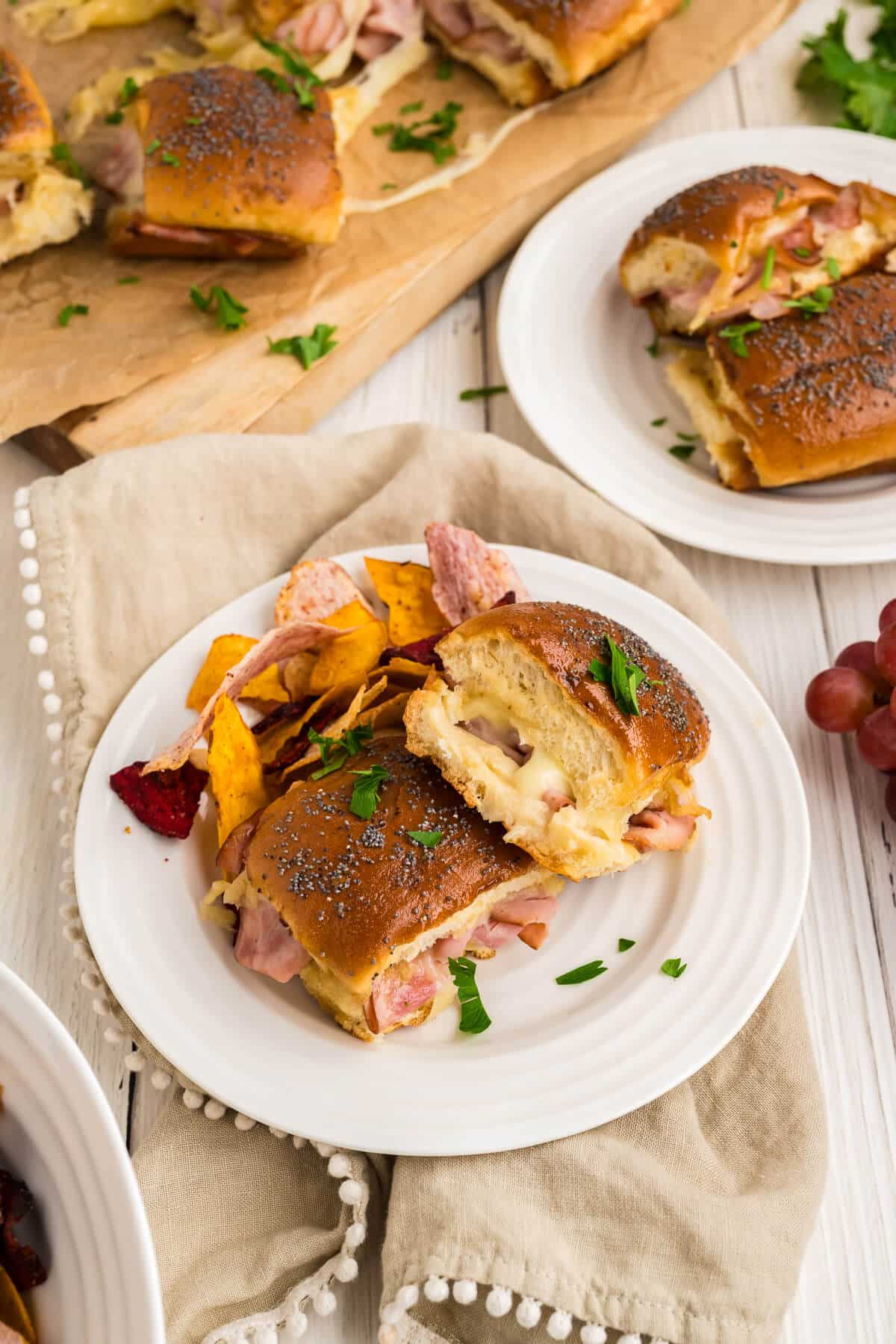 A couple ham and cheese sliders on a plate served with chips. 