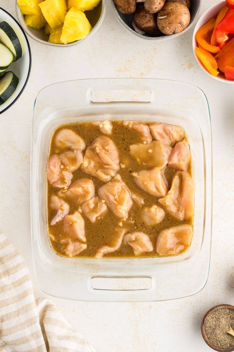 Chicken chunks marinating in shish kabob marinade in shallow dish.