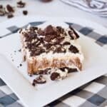 A slice of layered Oreo delight dessert on a white plate with a black and white checkered plate beneath.