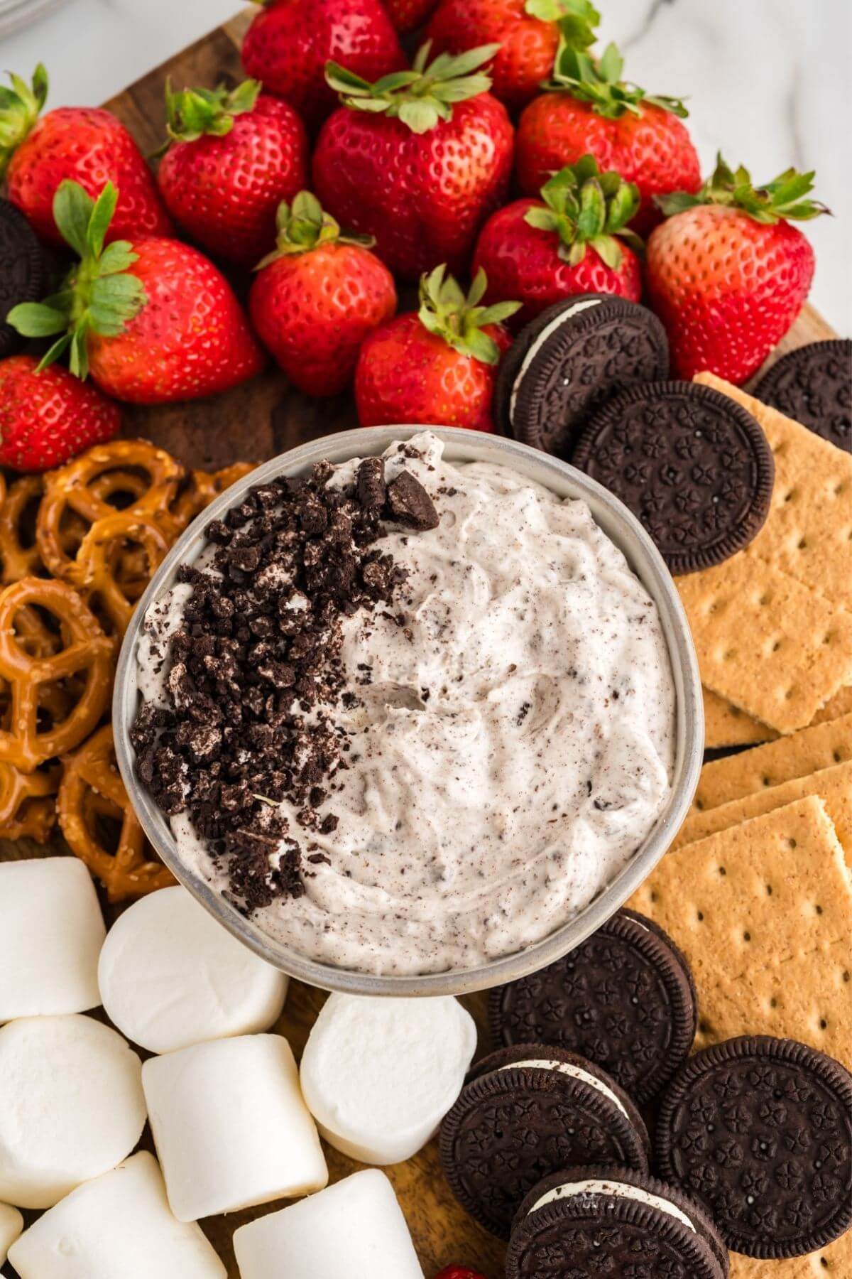 Bowl of oreo fluff dip on a tray filled with graham crackers, pretzels, strawberries, marshmallows.