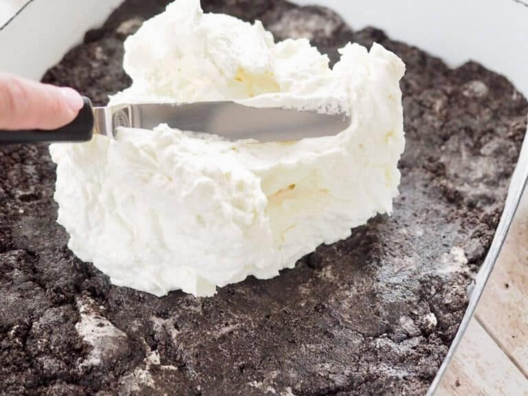 Spreading cream cheese and cool whip mixture on Oreo cookie crust.