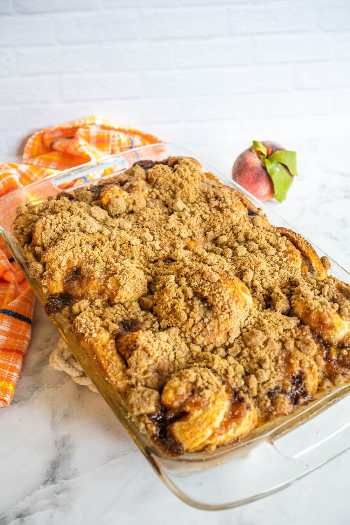 Peach Cobbler Cinnamon Rolls Crumb Topping on marble counter by peach.