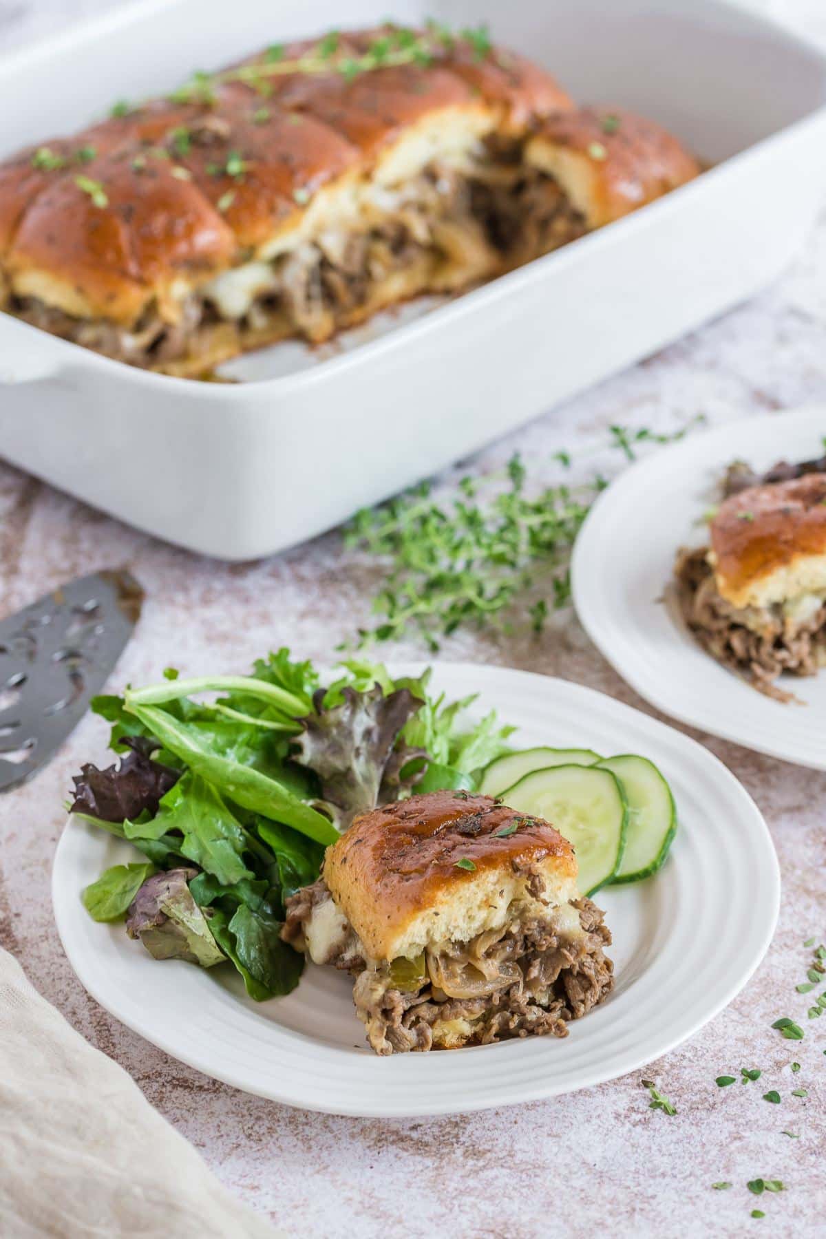 Philly Cheesesteak Slider on a plate with cucumbers and green salad.