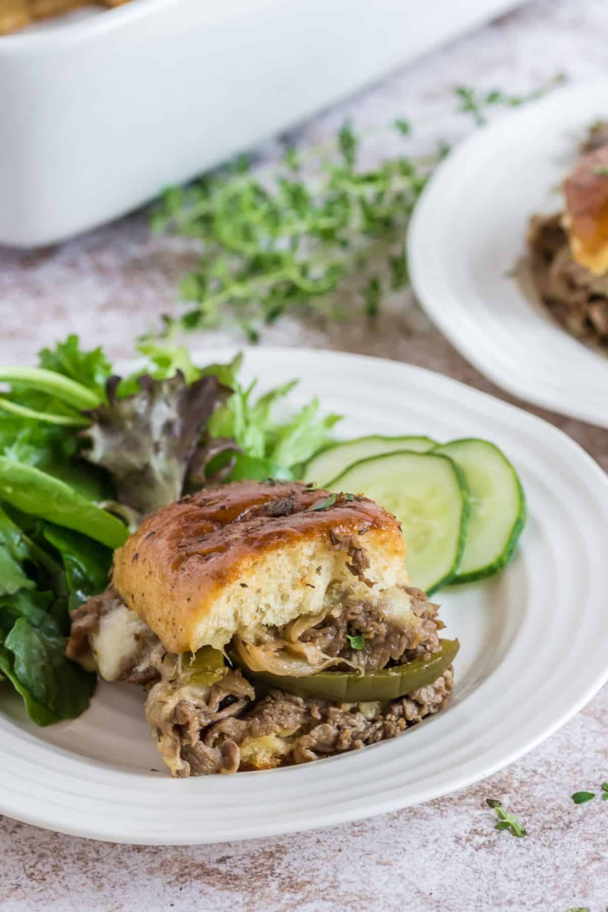 Philly Cheesesteak Sliders with slider on plate and salad and cucumbers.