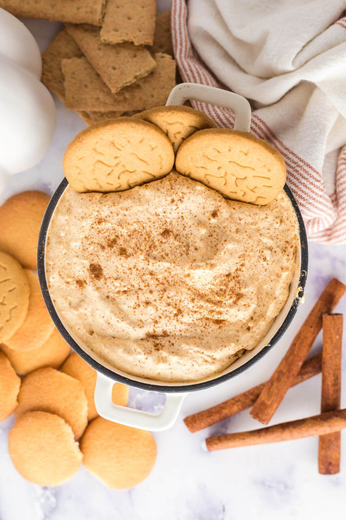 Pumpkin Fluff dip dessert with cookies artfully shown in dip and surrounding the bowl along with cinnamon sticks, graham crackers, and decorations.