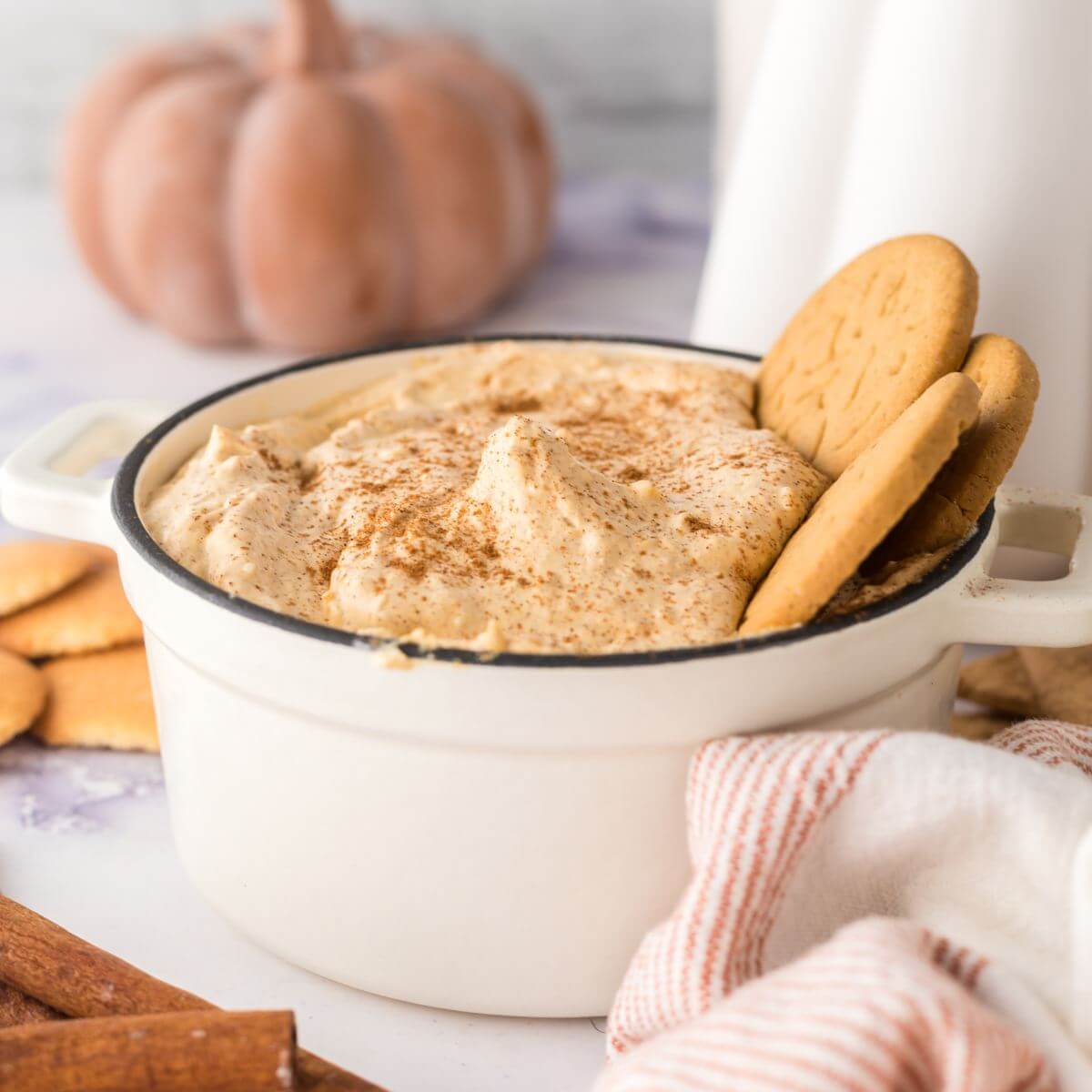 Square image of pumpkin fluff dip in a baking dish with cookies resting in the dip with a ceramic pumpkin in background.