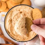 A hand dipping a cookie into the pumpkin fluff dip.