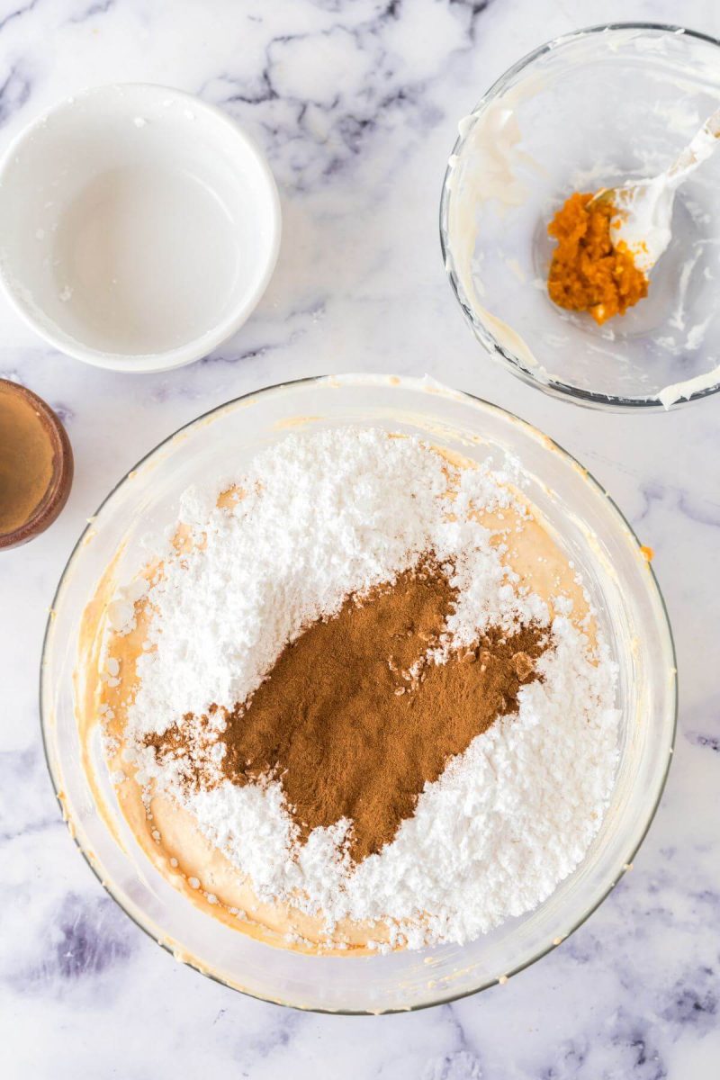 Pumpkin Fluff dip recipe showing powdered sugar and pumpkin pie spice or cinnamon added to mixture in bowl to blend.