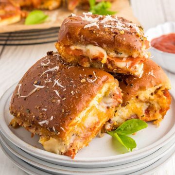 Pizza sliders stacked on plate with gooey cheese.