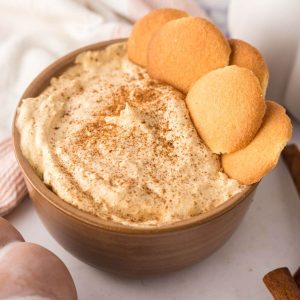 Square image of pumpkin fluff dip in bowl topped with pumpkin pie spice and cookies for dipping.