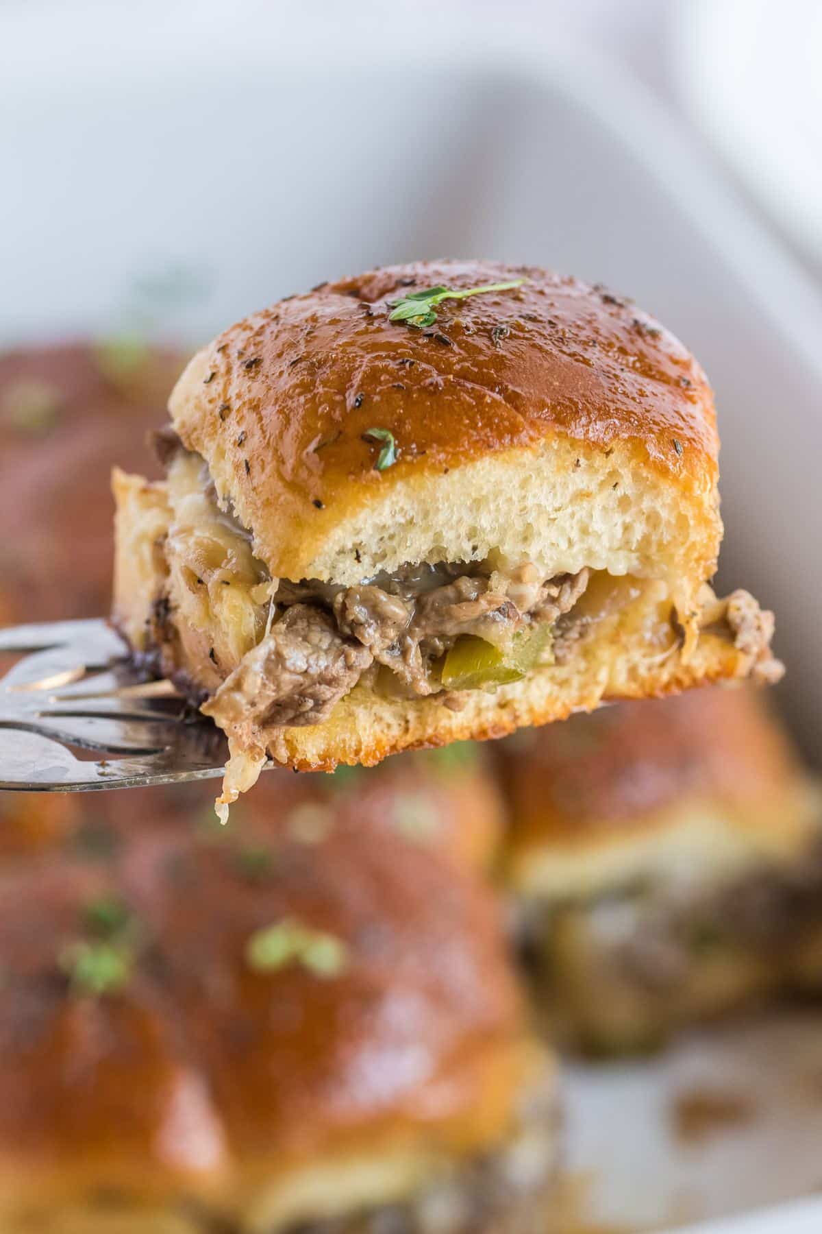 Steak slider on a serving spatula, with the pan full of Philly Sliders behind.