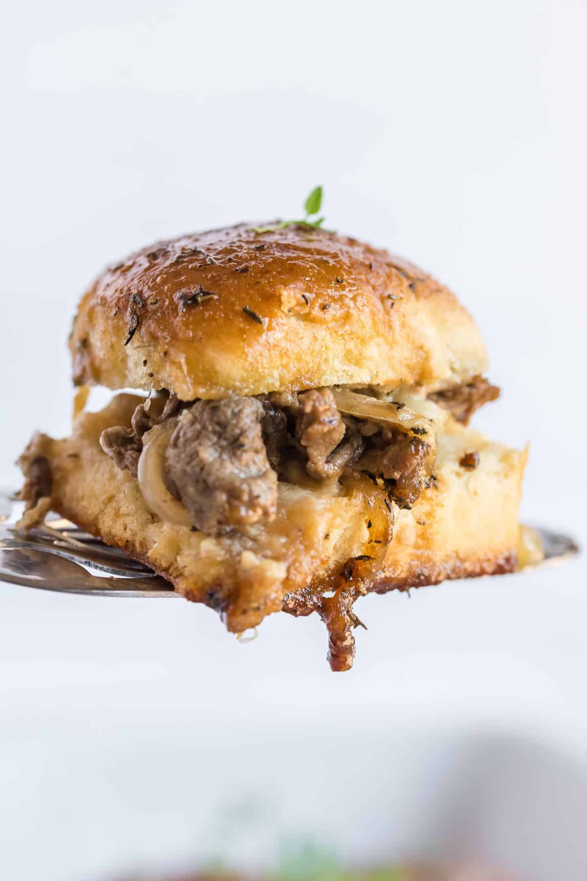 A steak slider on a serving spatula with dripping steak melty cheese.