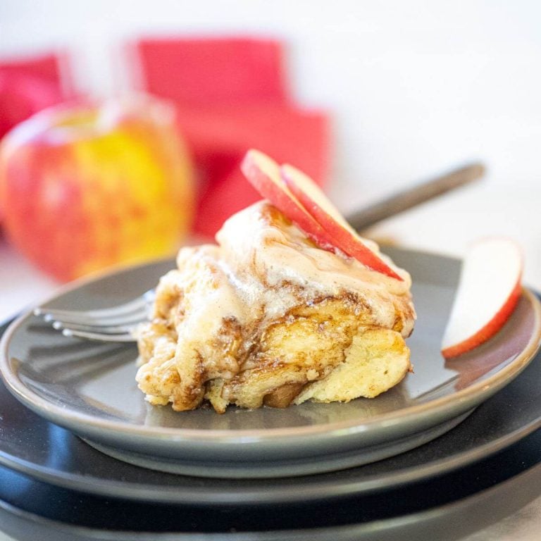 An apple cinnamon roll served on plate with apples.