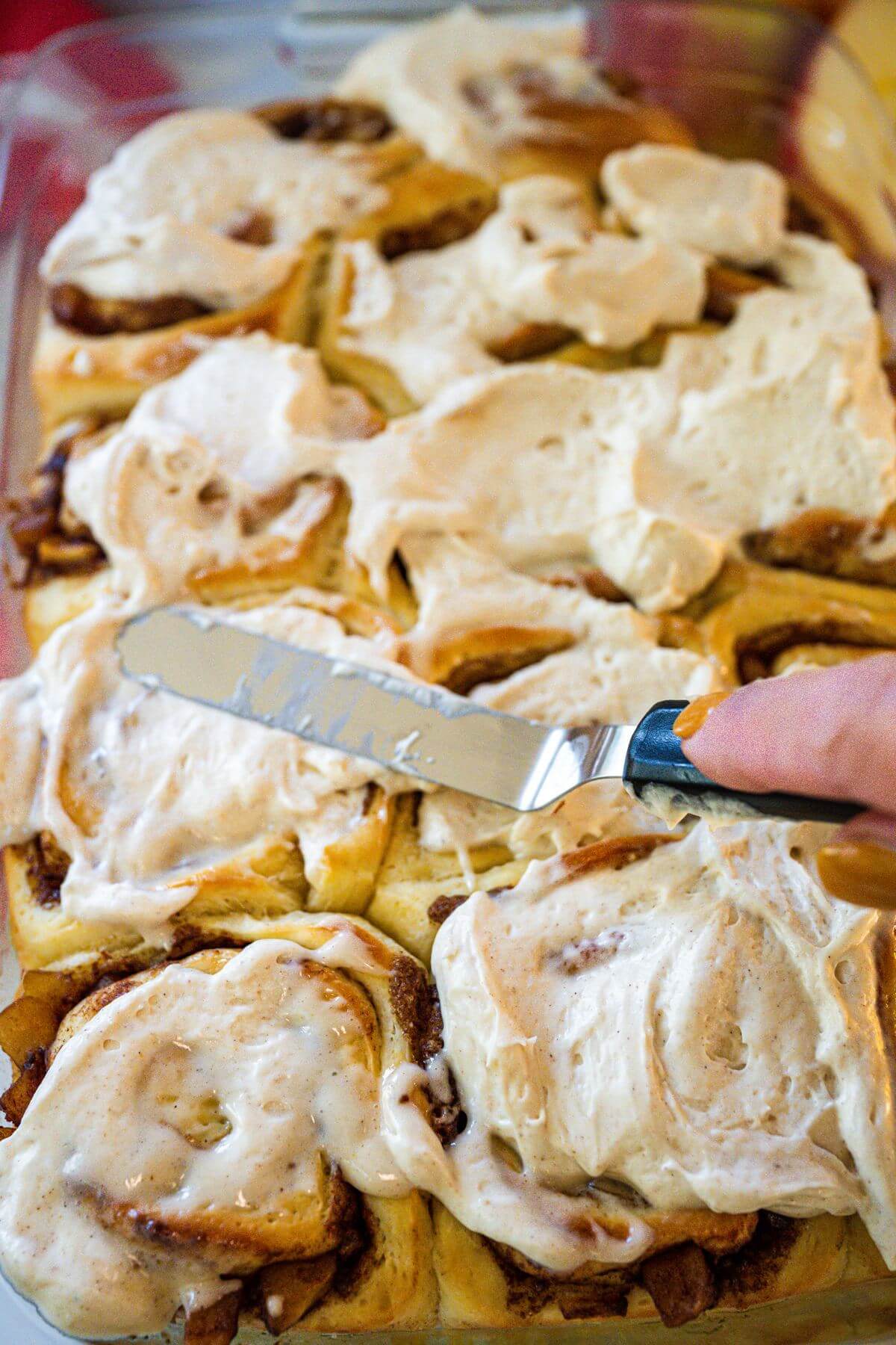 Someone is icing pan of cinnamon rolls with apple pie filling.