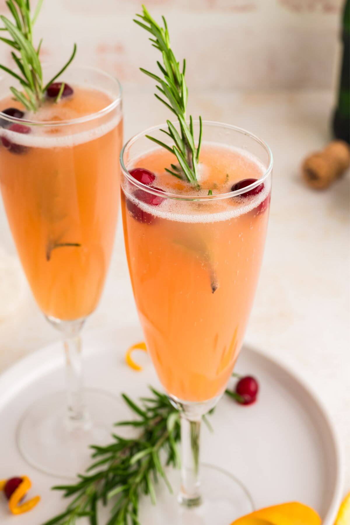 Two glasses of cranberry mimosa with rosemary garnish.