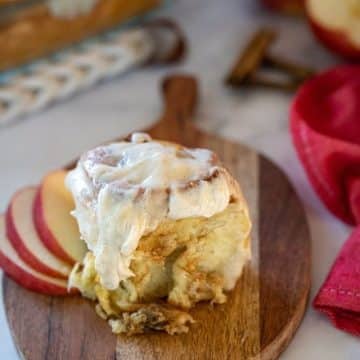 An apple pie cinnamon roll served on wooden board with apples.