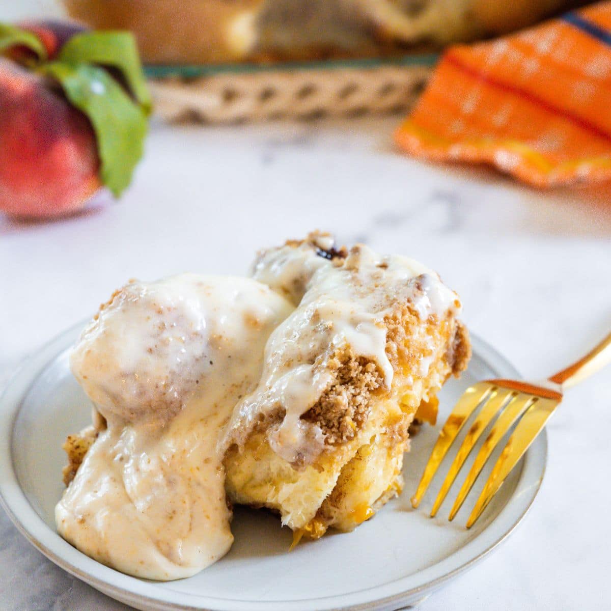 Gooey Peach Cobbler cinnamon roll on plate with melting peach cream cheese frosting.
