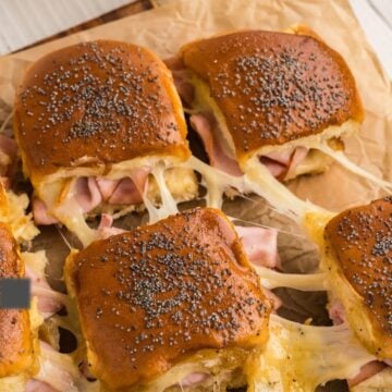 Ham and cheese sliders with stringy, gooey cheese on parchment paper.