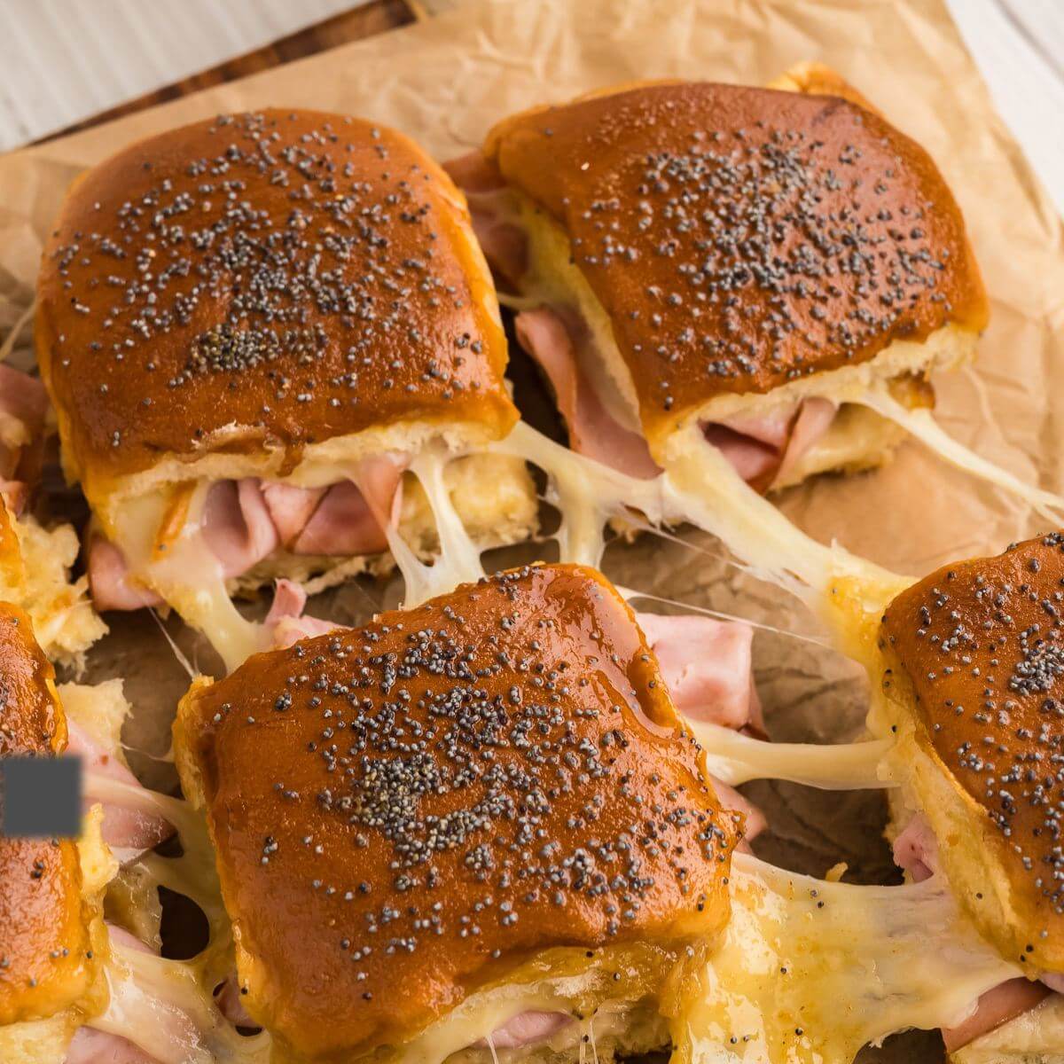 Ham and cheese sliders with stringy, gooey cheese on parchment paper.