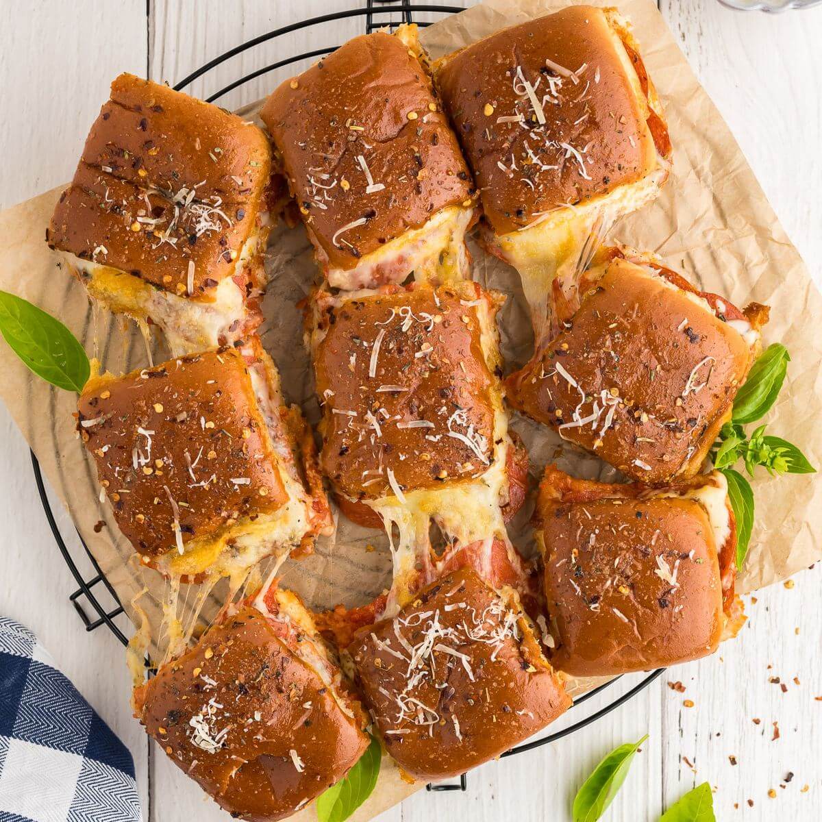 Square image of a plate with a three by three arrangement of pizza sliders connected by strings of melty cheese.