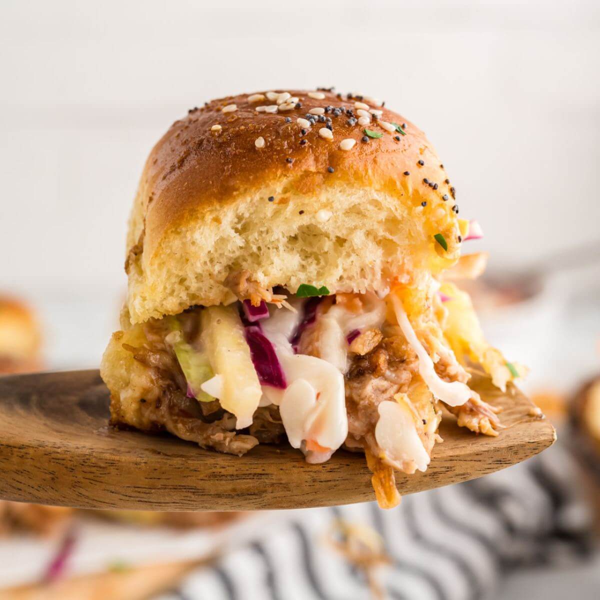 Pulled pork sliders recipe shown held up on wooden spoon.