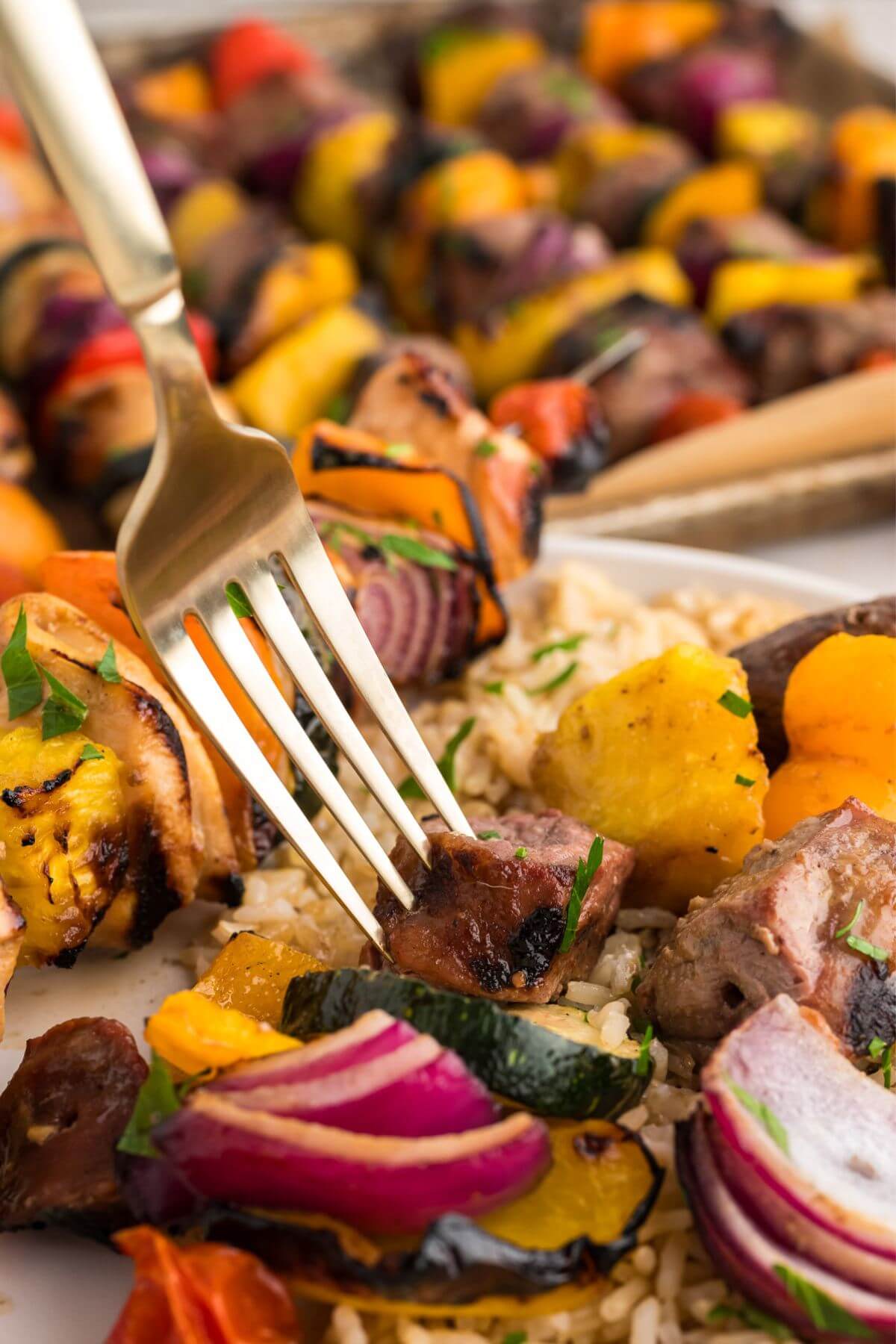 Close up photo of a fork stabbing a piece of marinated steak that was taken off of the skewer of the shish kebab, ready to eat.