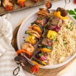 Two skewered shish kababs with steak and chicken, vegetables on a bed of rice.