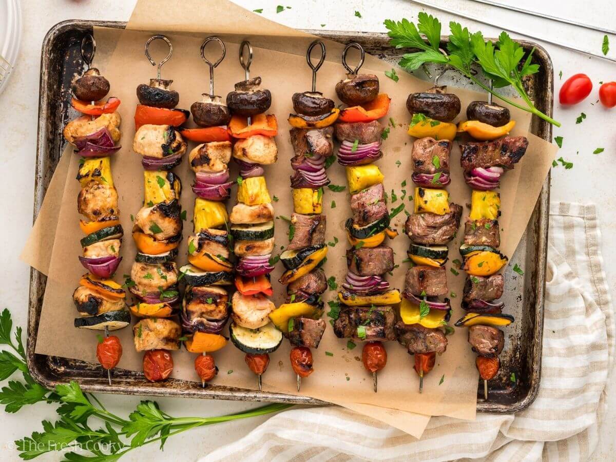 Shish kabobs both chicken and steak grilled and with veggies on a parchment lined tray.