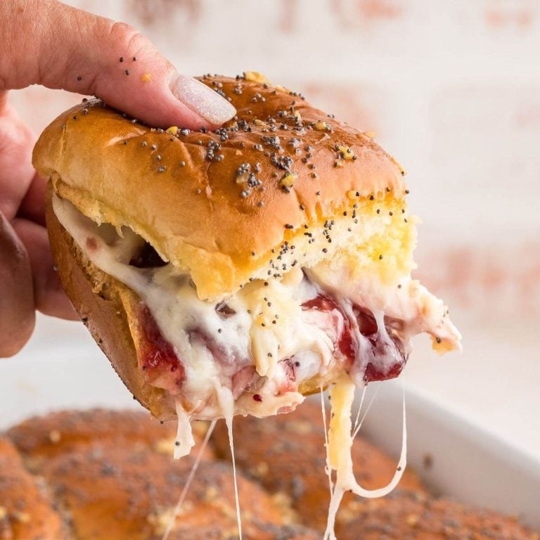 Hand lifting up a turkey, cranberry and cheese slider showing ooey gooey cheese stringing from the pan.
