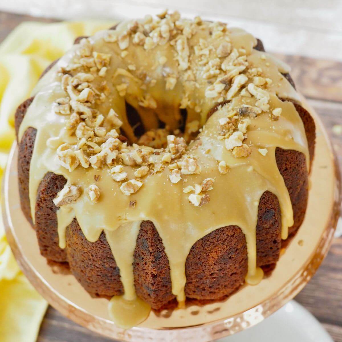 Close up of whole Banana Bread Bundt Cake with sauce and walnuts on platter.